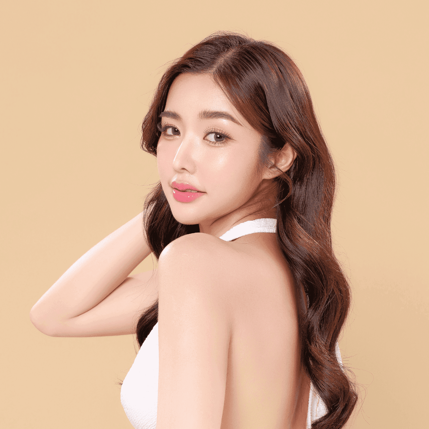 Woman with long wavy hair in white top, looking back over shoulder on beige background.